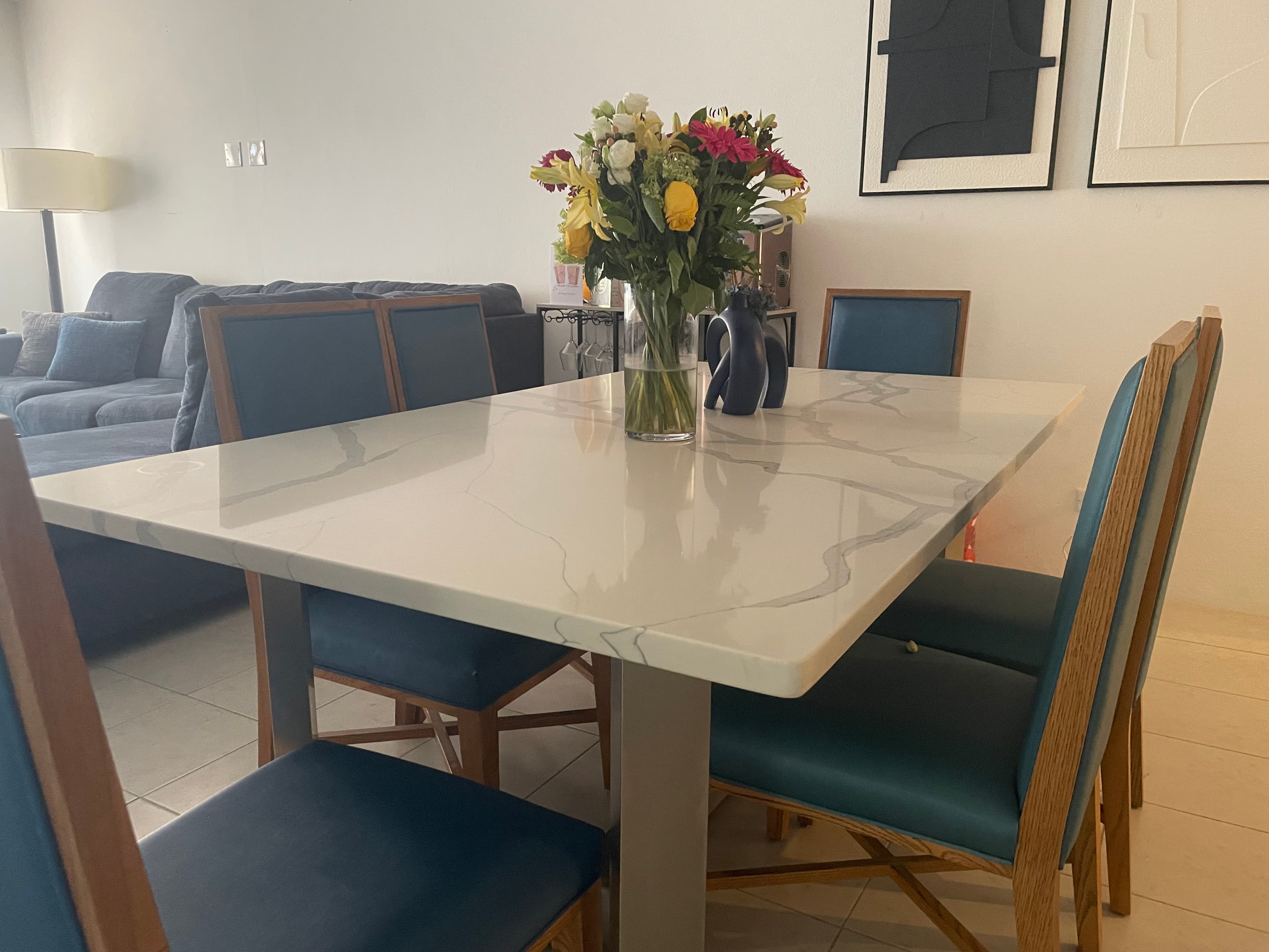 Modern white marble dining table with blue chairs and a colorful bouquet of fresh flowers.